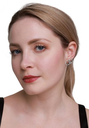 Silberne Creolen mit verflochtenem Design, glatter Textur und dezentem Glanz, getragen von einem Model mit heller Haut und glattem Haar.