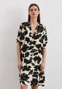Abito a maniche corte color crema con stampe floreali nere, dotato di colletto e dalla vestibilità ampia. Il tessuto ha una superficie liscia.