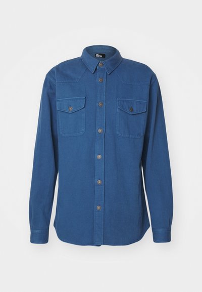 Camicia blu a maniche lunghe realizzata in tessuto morbido, con colletto classico, chiusura frontale con bottoni, due tasche sul petto e dettagli testurizzati.