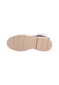 Le calzature presentano una suola in gomma beige con scanalature orizzontali, una tomaia sintetica color tan e una cinghia strutturata realizzata in materiale peloso bianco sporco.
