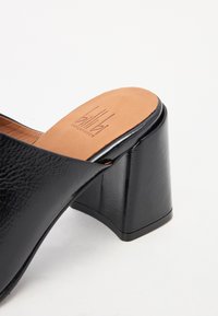 Sandal con tacco nero, dotato di una tomaia in pelle texturizzata e un ampio tacco a blocco. La soletta è color beige ed è impreziosita da un logo impresso al centro.