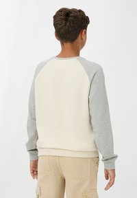 Felpa raglan crema e grigia con texture morbida, polsini a coste e scollatura tonda, abbinata a pantaloni cargo color khaki.