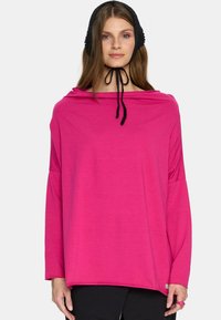 Jasnoróżowa bluzka z długim rękawem o luźnym kroju, szerokim dekolcie i czarnym sznurkiem. Miękka tkanina i minimalistyczny design, połączone z czarnymi spodniami.