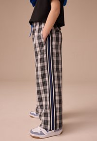 Pantalon à carreaux noir et blanc avec des accents rayés bleus sur les côtés, doté d'une taille à cordon et de poches, assorti à des baskets blanches et bleues.