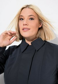 Giacca nera con colletto alto e design strutturato. Tessuto morbido con cuciture sottili e silhouette aderente.