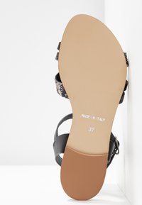 Sandale à brides avec une bride de cheville en cuir noir, empeigne texturée grise/noire à motif, et semelle en caoutchouc beige. Marquée "Made in Italy" et taille 37.