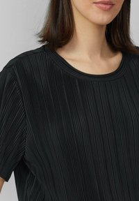 Zwart geplooid top met een ronde halslijn, korte mouwen en een textiel met verticale lijnen.