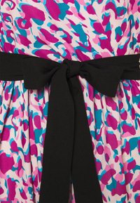 Mönstrad tyg har abstracta former i rosa, lila och blått, med ett solid svart knytbälte i midjan som skapar en åtdragen look.