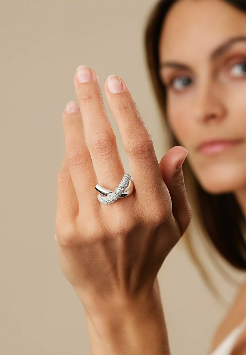 Anello d'argento con un design attorcigliato, che presenta una fila di piccole pietre trasparenti. Indossato su una mano con pelle chiara su uno sfondo neutro.