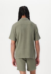 Olijfgroene, kortekorte mouwenshirt en bijpassende korte broek van gestructureerde stof. Voorzien van een button-down kraag en een relaxte pasvorm.
