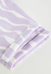 Lila szövet, fehér hullámos csíkokkal, látható varrással és puha textúrával. Az anyag könnyűnek és rugalmasnak tűnik.