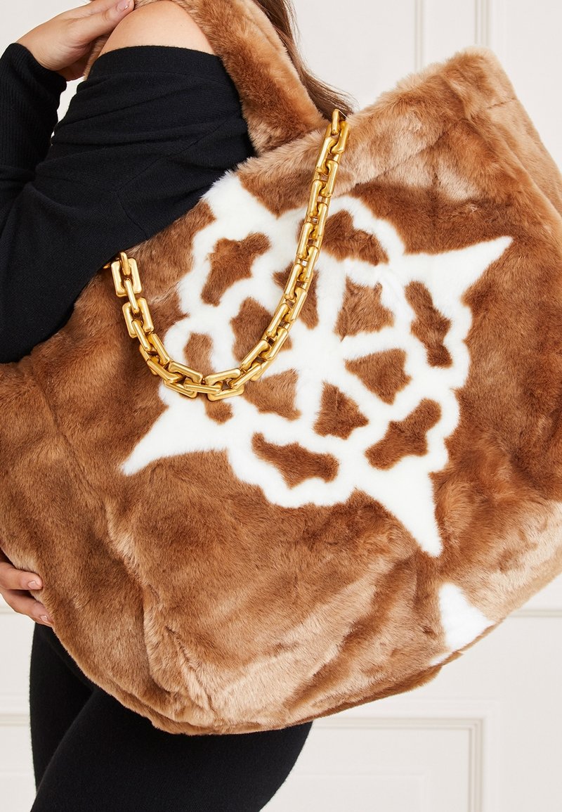 Brązowa torba tote z futerkiem syntetycznym w białe gwiazdy, z złotym łańcuszkiem i miękką, teksturowaną powierzchnią.