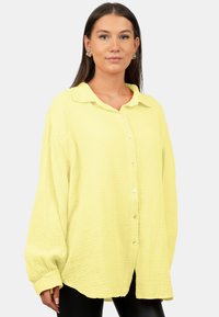 Camicia button-up gialla chiara in tessuto testurizzato e stropicciato, con colletto, maniche lunghe e vestibilità ampia, che evidenzia sottili dettagli dei bottoni.