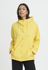 Veste imperméable jaune avec capuche, boutons-pression argentés et cordons blancs. Comprend des poches latérales et un design décontracté.