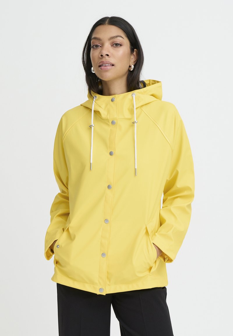 Veste imperméable jaune avec capuche, boutons-pression argentés et cordons blancs. Comprend des poches latérales et un design décontracté.