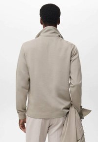 Suéter beige texturizado con cuello alto, mangas largas y un ajuste relajado, mostrado en una persona de espaldas.