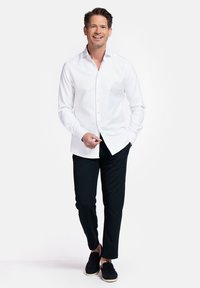 Witte overhemdbloes met lange mouwen, gecombineerd met donkergekleurde broek en zwarte instappers. Heeft een ontspannen pasvorm en een soepele textuur.