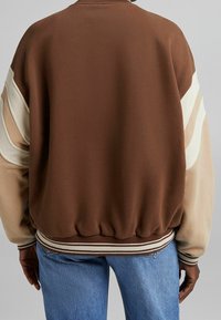 Brun sweatshirt med krämfärgade och ljusbruna accentremsor. Ribbade midja och ärmslut, avslappnad passform, mjuk textur och rund halsringning.