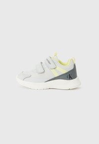 Gray athletic shoe with yellow accents and velcro strap closures. Features a textured sole and distinct branding on the side.