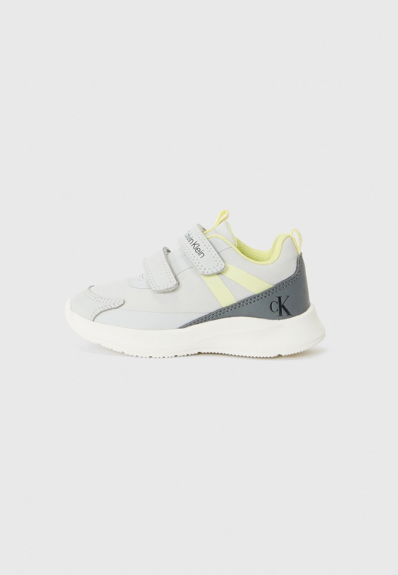 Gray athletic shoe with yellow accents and velcro strap closures. Features a textured sole and distinct branding on the side.