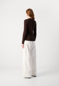 Pull en tricot marron avec des manches longues, silhouette ajustée. Assorti avec un pantalon blanc ample taille haute, vu de dos.
