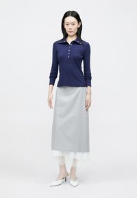 Polo a maniche lunghe blu navy con bottoni e colletto, abbinato a una gonna lunga grigia con orlo in pizzo e tacchi bianchi. Design minimale.