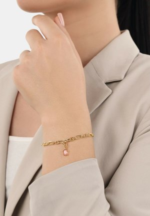 Bracciale in oro con grandi maglie, con un charm in pietra rosa. Indossato su un polso, che mette in mostra un design del gancio liscio.