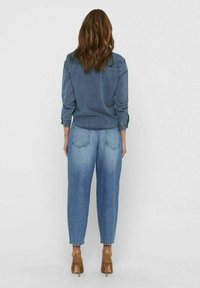 Camicia di denim blu scuro con maniche lunghe, abbinata a jeans a sigaretta blu chiaro. I tacchi sono marroni e l'outfit è visto da dietro.