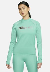 Maglia atletica a maniche lunghe verde menta con colletto alto, caratterizzata da un grande logo metallico "nike AIR" sul petto e maniche raglan.