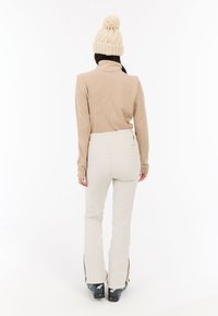 Beige gestreepte langmouwen top in combinatie met crèmekleurige skibroek. De outfit heeft een aansluitend design, met ritsen bij de broekspijpen.