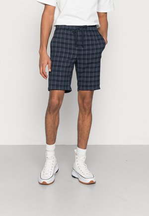Marineblauwe geruite shorts met een tailleband met trekkoord, zijzakken en een losse pasvorm. Gecombineerd met witte hoge sneakers en crew-sokken.