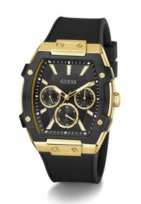 Montre à bracelet en caoutchouc noir avec un boîtier en or, design géométrique, cadran texturé noir, trois sous-cadrans et accents dorés. Présente de grands index horaires.