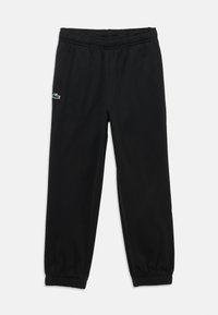 Pantalon de survêtement noir en tissu doux avec une taille élastique. Présente des poignets côtelés et un petit logo vert Lacoste sur le côté gauche.