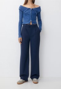 Modrý žebrovaný top bez ramínek s předním zipem, skombinovaný s tmavě námořnickými kalhotami s vysokým pasem a šedými teniskami.