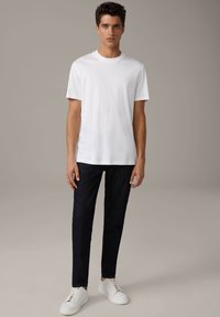 T-shirt bianco in cotone con maniche corte, abbinato a pantaloni in denim scuri e sneakers bianche. Taglio semplice e classico senza motivi visibili.