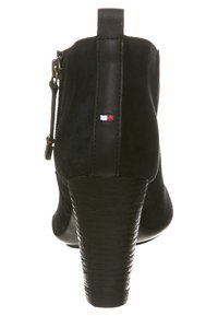 Czarny zamszowy botek za kostkę z wysokim, fakturowanym obcasem i suwakiem. Z tyłu znajduje się małe trójkątne logo w kolorze.