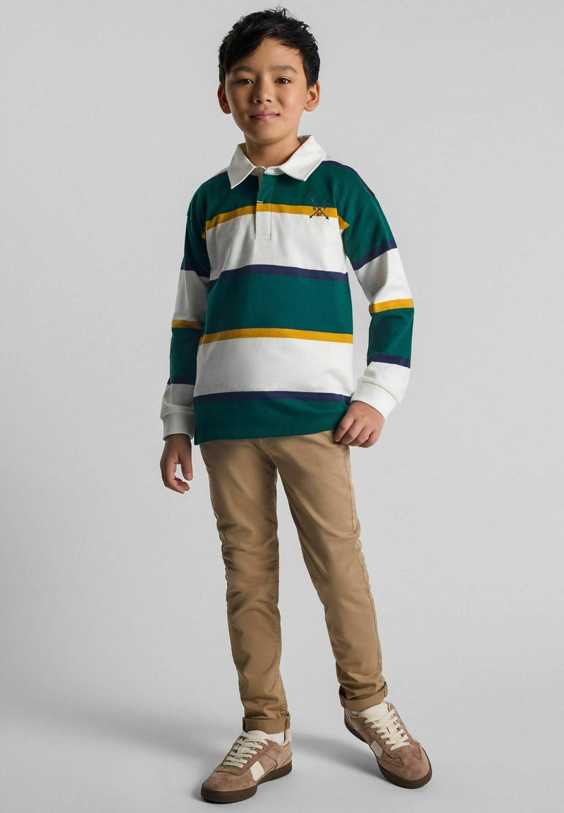 Groen, wit en geel gestreepte lange mouwen polo-shirt gecombineerd met beige slim-fit broeken en bruine sneakers met witte accenten.