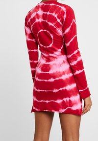 Vestido de tie-dye rojo con mangas largas, que presenta patrones circulares en tonos de rosa, fabricado en un tejido suave y con una silueta ajustada.