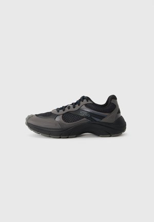 Sportliche Sneakers in Schwarz und Grau mit einem atmungsaktiven Mesh-Obermaterial, gepolstertem Schaft und strukturiertem Gummisohle. Mit Branding an der Seite.
