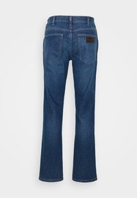 Los pantalones vaqueros acampanados de color azul oscuro cuentan con un diseño clásico de cinco bolsillos, costuras de contraste y una etiqueta de cuero en la parte posterior de la cintura. Textura de denim suave.