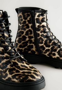 Leopardmønstrede ankelstøvler med sorte snørebånd og lynlås, der har en glat tekstur og en robust sort sål. Synlige syninger og øjer.