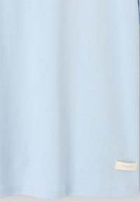 Tissu bleu clair avec une petite étiquette rectangulaire blanche cousue près de l'ourlet inférieur du côté droit.