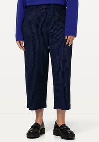 Pantalones cortos de color azul marino con patrón de houndstooth texturizado, cintura alta y piernas anchas, combinados con zapatos negros de suela gruesa.