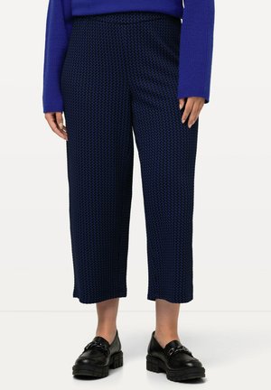 Marineblaue cropped Hose mit strukturiertem Hahnentritt-Muster, hoher Taille und weitem Bein, kombiniert mit schwarzen Schuhen mit dicker Sohle.