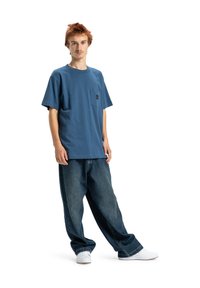 Blue cotton t-shirt with short sleeves and a chest pocket, paired with loose-fitting dark denim jeans and white sneakers.