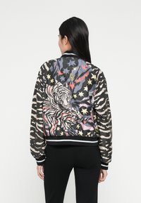 Chaqueta bomber con tejido negro con estampados de tigre y estrellas, mangas rayadas en contraste, puños y dobladillo acanalados, y un ajuste relajado.