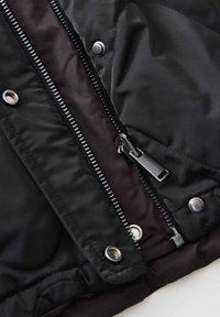 Veste doudoune noire au design épuré, avec fermeture éclair à glissière métallique, pressions et doublure intérieure contrastante sombre.