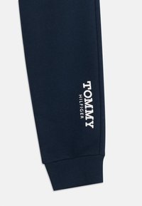 Σκούρες μπλε φόρμες με ribbed μανσέτες, που φέρουν ένα λευκό λογότυπο που γράφει "TOMMY HILFIGER" στην αριστερή πλευρά. Μαλακή υφή υφάσματος.