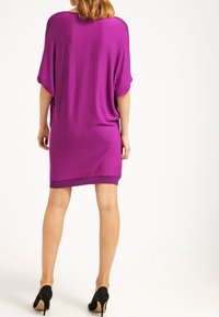 Lila stickad klänning med avslappnad passform, korta ärmar och en solid nederkant. Bärs med svarta högklackade skor.