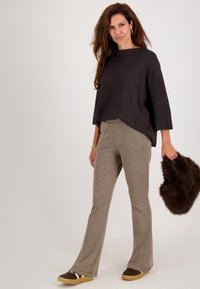 Boxy zwart sweater, beige broek met een houndstooth-patroon, en een bruine bont clutch. Bruine sneakers met witte accenten. Eenvoudig, textuurvol ontwerp.